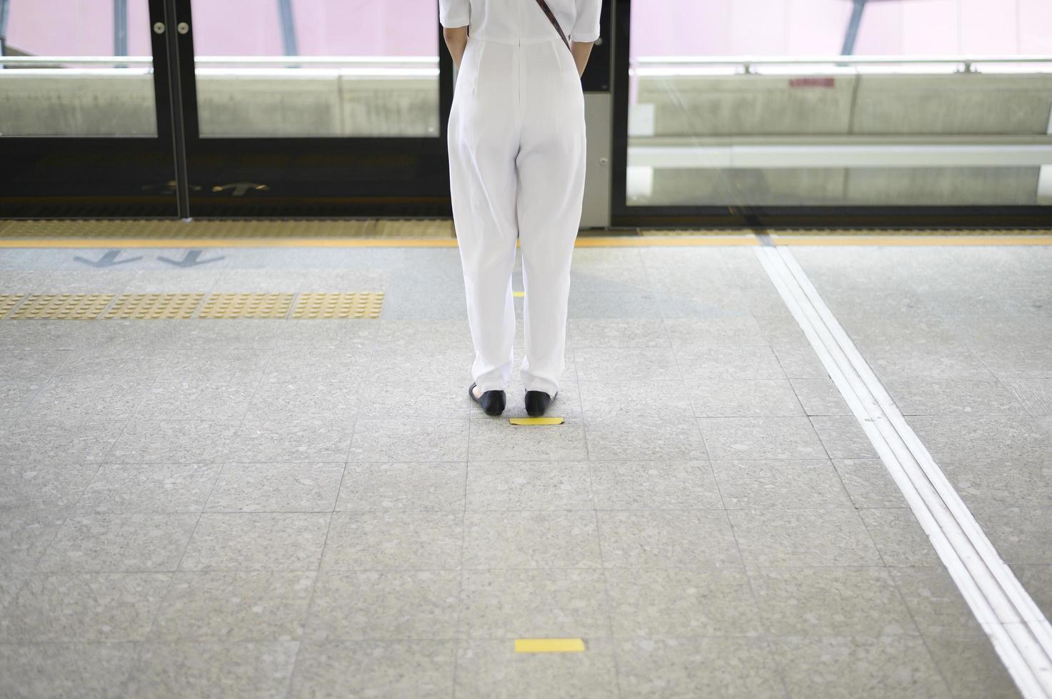 una giovane donna è in piedi sulla piattaforma della metropolitana, indossa una maschera facciale, protezione covid-19, nuovo concetto di viaggio normale. foto