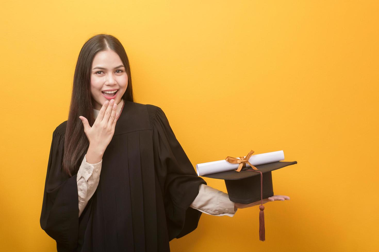 ritratto di bella donna felice in abito di laurea è in possesso di certificato di istruzione su sfondo giallo foto