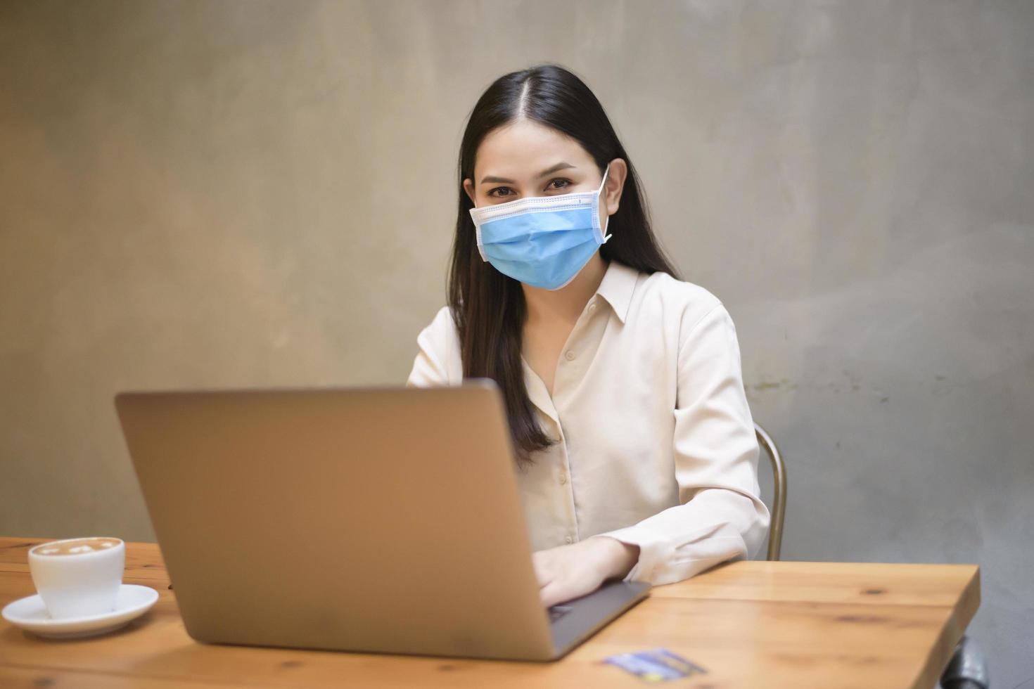 bella donna con maschera sta lavorando su un computer portatile in caffetteria foto