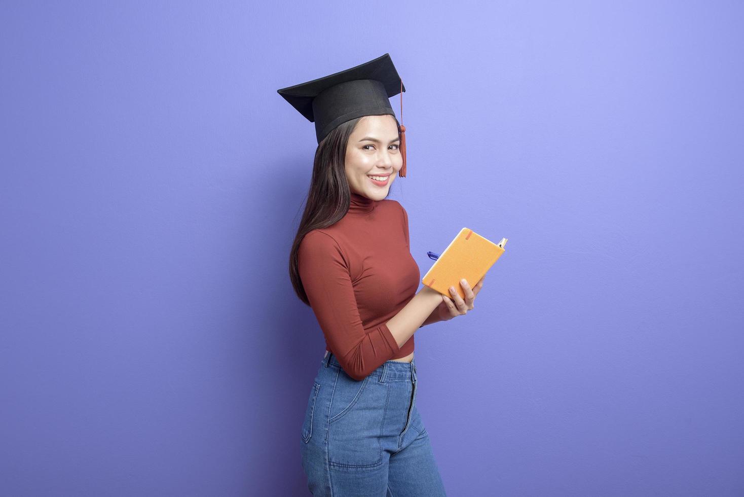 ritratto di giovane studentessa universitaria con cappuccio di laurea su sfondo viola foto