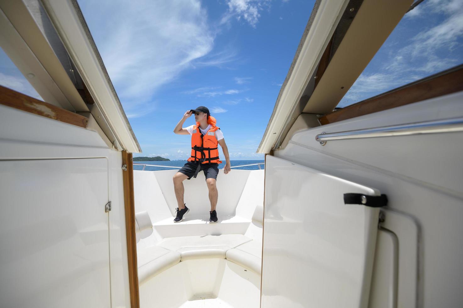 turista in giubbotto di salvataggio che si diverte e si rilassa sul motoscafo con una splendida vista sull'oceano e sulle montagne sullo sfondo foto