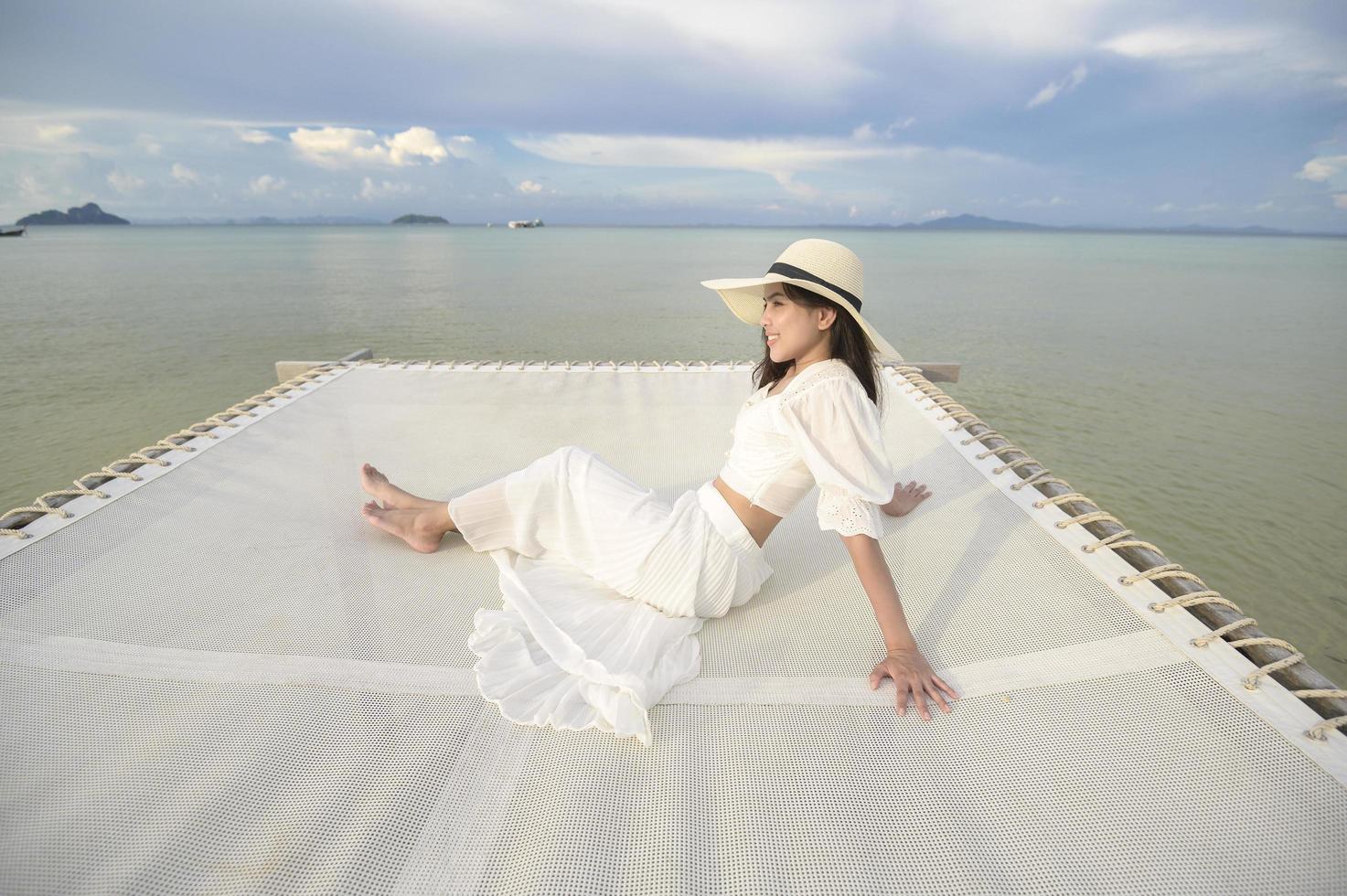 una bella donna felice in abito bianco che si gode e si rilassa sulla terrazza dell'isola tropicale e dell'oceano turchese, dell'estate e delle vacanze foto