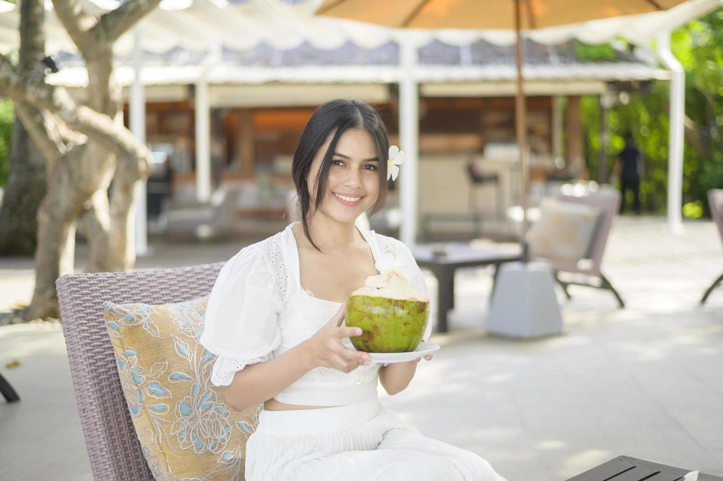 bella turista con fiore bianco sui capelli che beve cocco seduto sulla poltrona durante le vacanze estive foto