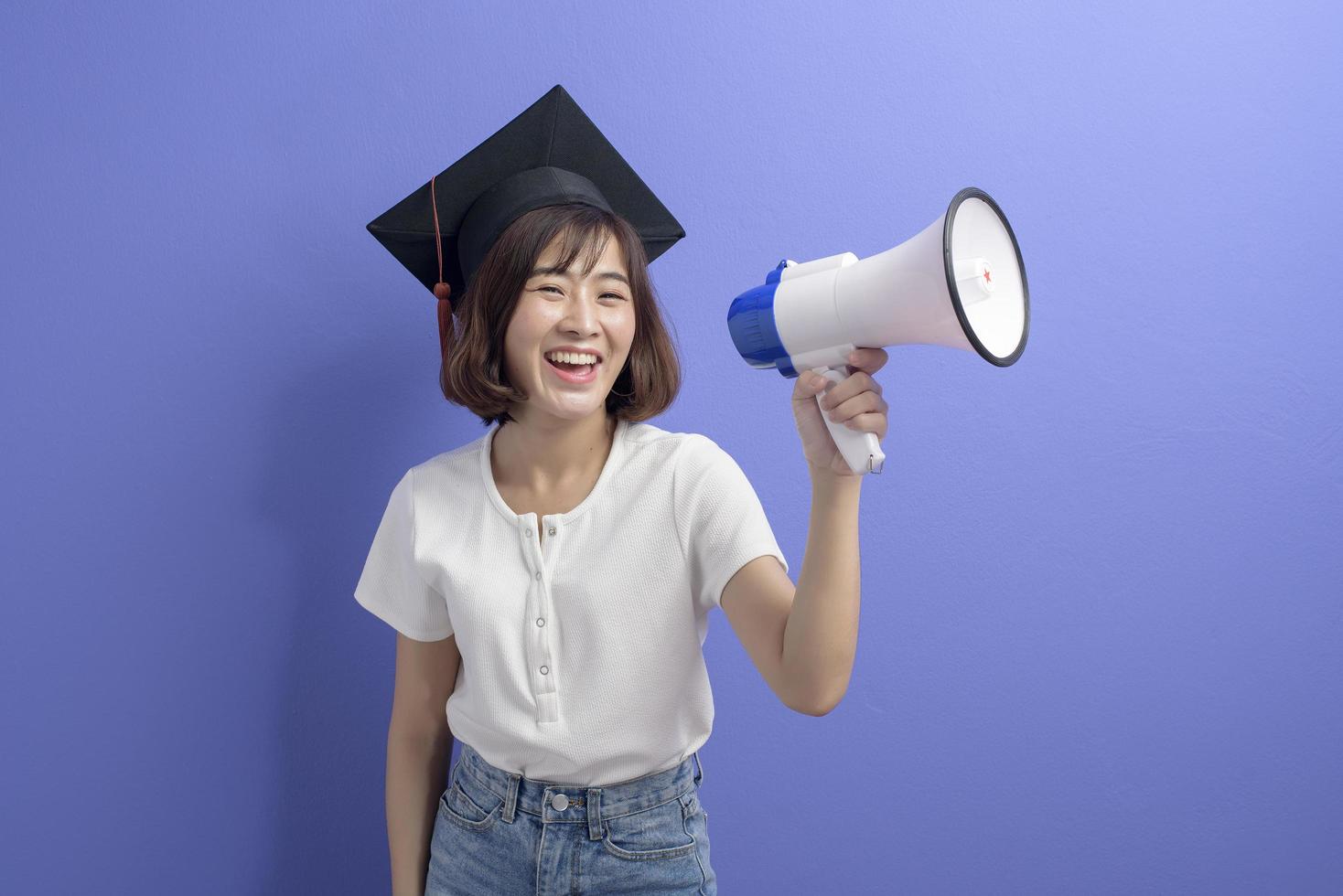 ritratto di studente asiatico laureato in possesso di megafono isolato sfondo viola studio foto