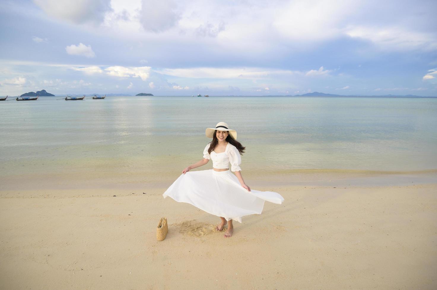 una bella donna felice in abito bianco che si gode e si rilassa sul concetto di spiaggia, estate e vacanze foto