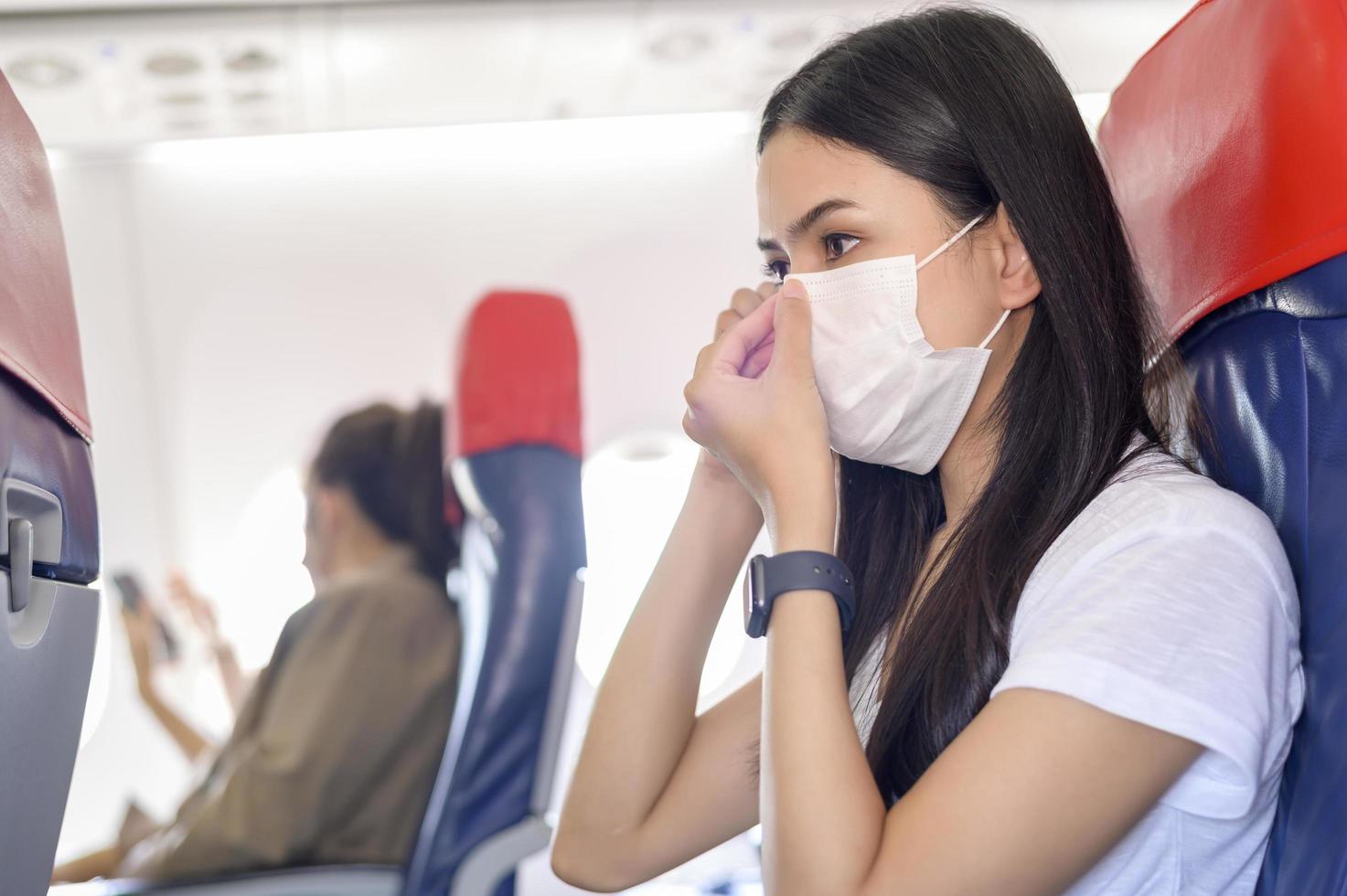 la donna in viaggio indossa una maschera protettiva a bordo dell'aereo, viaggia in condizioni di pandemia covid-19, viaggi di sicurezza, protocollo di allontanamento sociale, nuovo concetto di viaggio normale foto