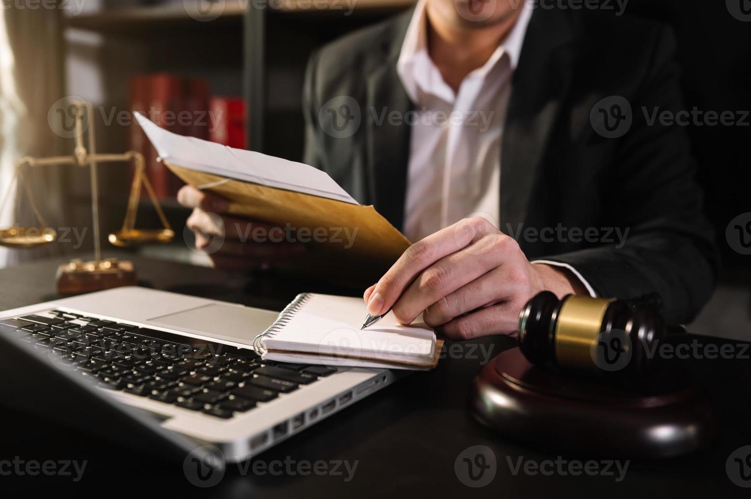 concetto di giustizia e diritto. giudice maschio in un'aula di tribunale con il martelletto, lavorando con computer e tastiera docking, occhiali, sul tavolo alla luce del mattino foto