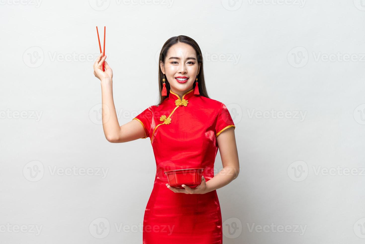 bella donna asiatica nel tradizionale abito cinese rosso qipao con scatola di plastica per alimenti e bacchette in studio isolato su sfondo grigio foto