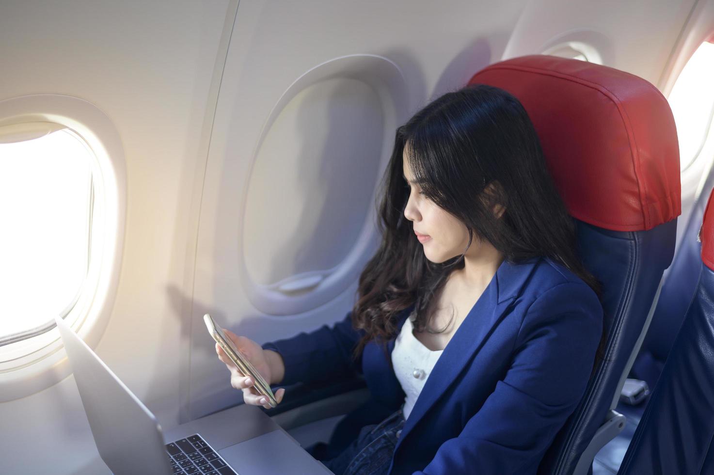 una giovane donna d'affari che indossa un abito blu sta usando il laptop a bordo foto