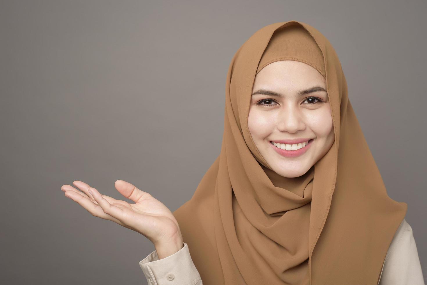 ritratto di bella donna con hijab sta mostrando qualcosa sulla sua mano su sfondo grigio foto