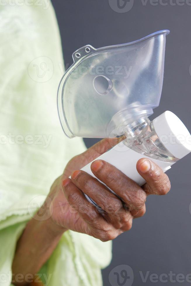 le donne anziane tengono in mano un nebulizzatore su sfondo grigio chiaro foto