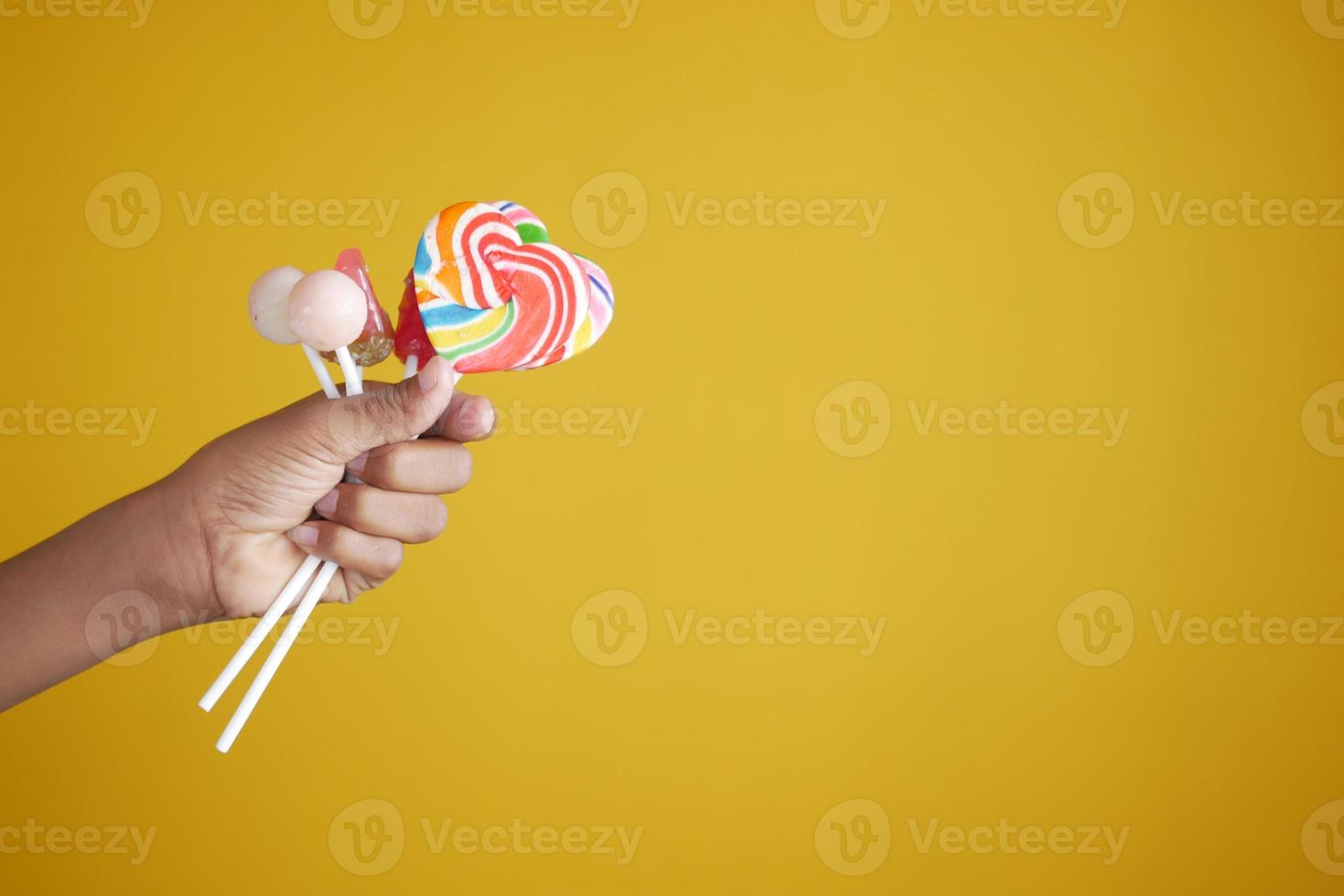 bambino che tiene lecca-lecca a forma di cuore arcobaleno su sfondo giallo foto