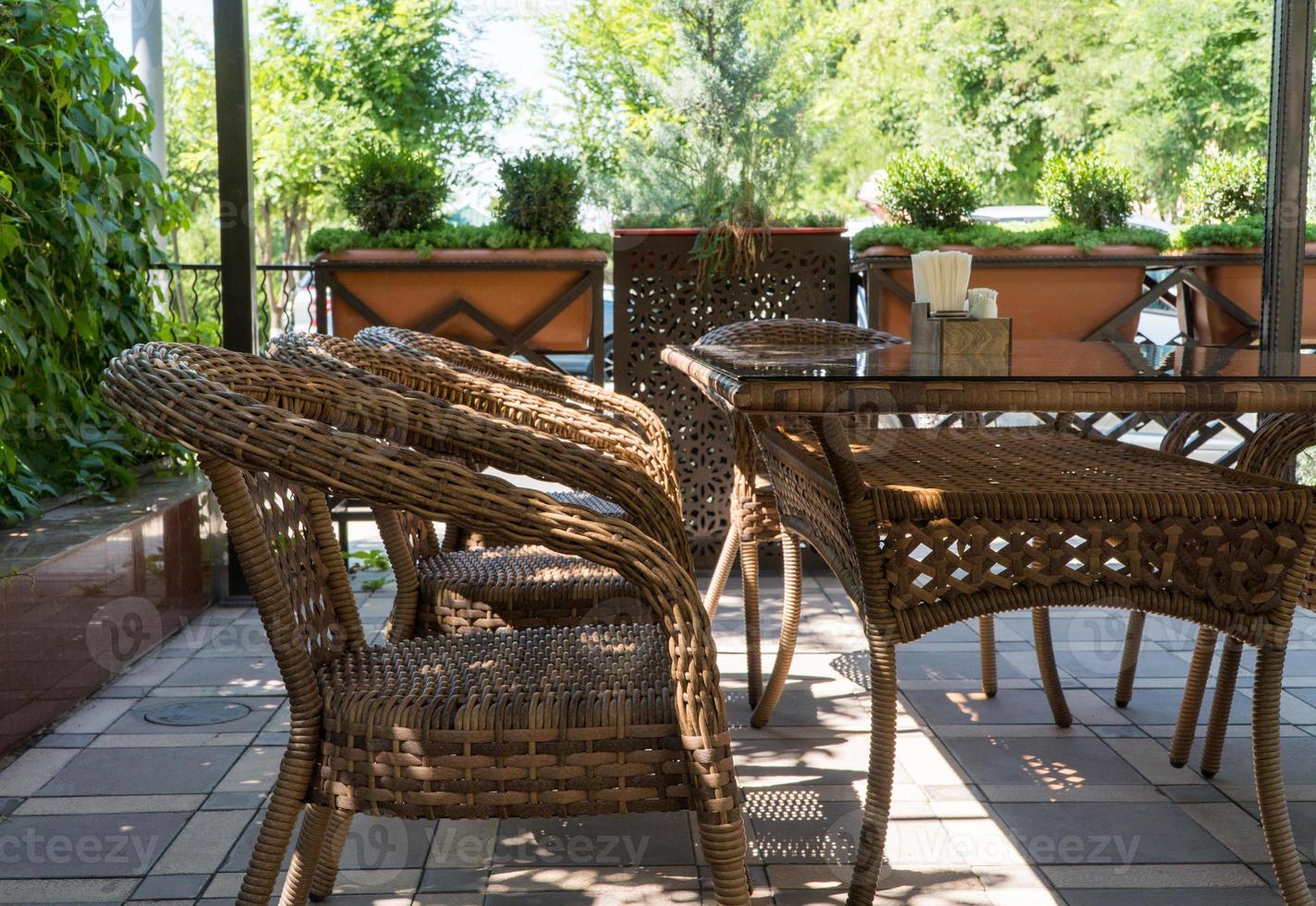 tavoli e sedie di vimini nella caffetteria estiva all'aperto con aiuole foto