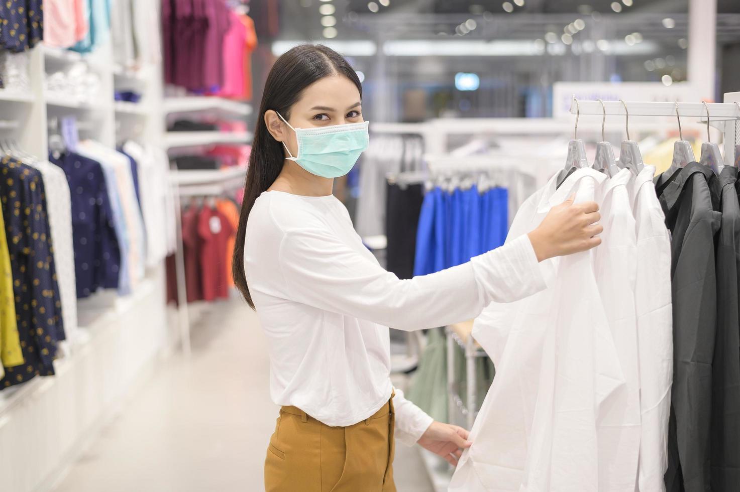 donna che indossa una maschera protettiva che acquista sotto la pandemia covid-19 nel centro commerciale, protocollo di allontanamento sociale, nuovo concetto normale. foto