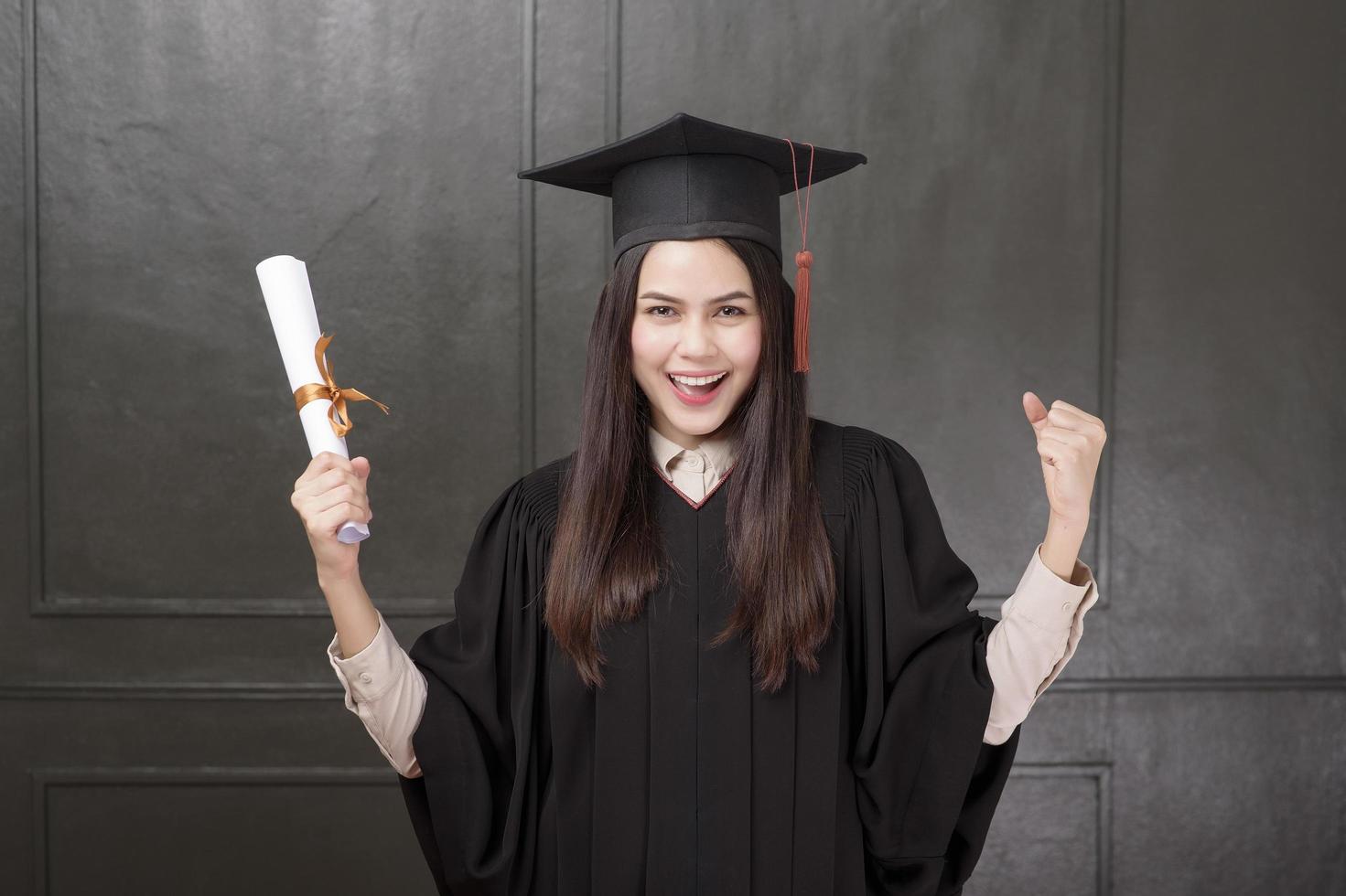 ritratto di giovane donna in abito di laurea sorridente e tifo su sfondo nero foto