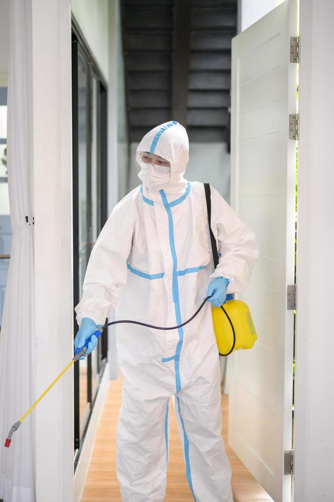 uno staff medico in tuta dpi sta usando spray disinfettante in soggiorno, protezione covid-19, concetto di disinfezione. foto