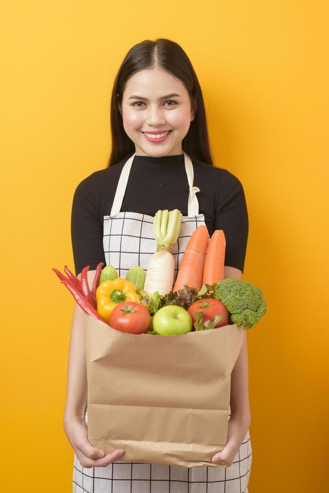 bella giovane donna sta tenendo le verdure nel sacchetto della spesa in studio sfondo giallo foto