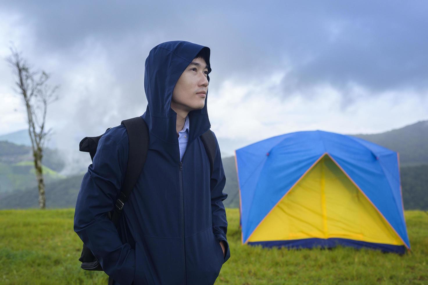 uomo di viaggio felice che si diverte e si rilassa vicino alla tenda del campo sulla bellissima montagna verde nella stagione delle piogge, clima tropicale. foto