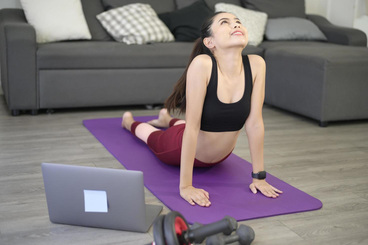 una giovane donna felice in abbigliamento sportivo sta facendo stretching e riscaldamento sul tappetino in soggiorno a casa foto