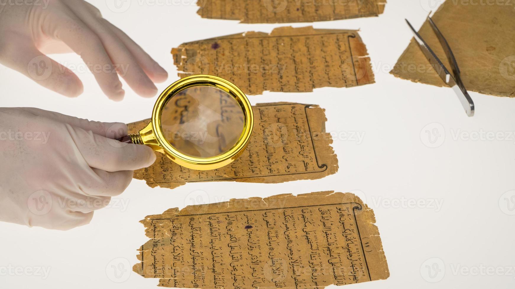 un ricercatore studia la scrittura araba dal Corano usando una lente d'ingrandimento e un tavolo con una luce. paleografia, lo studio della scrittura araba antica foto