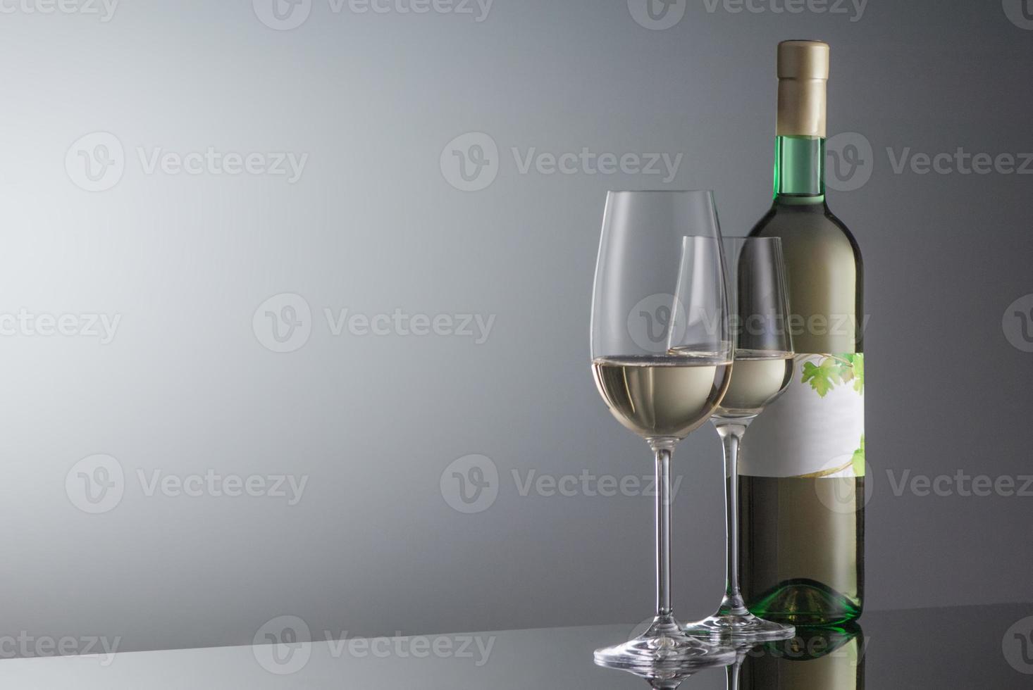 bottiglia di vino bianco con bicchiere di vino su sfondo grigio con illuminazione foto