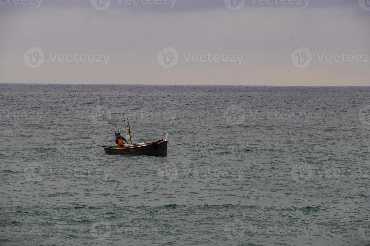 un pescatore e la sua barca lungo la costa del mare ligure, mentre inizia a pescare foto