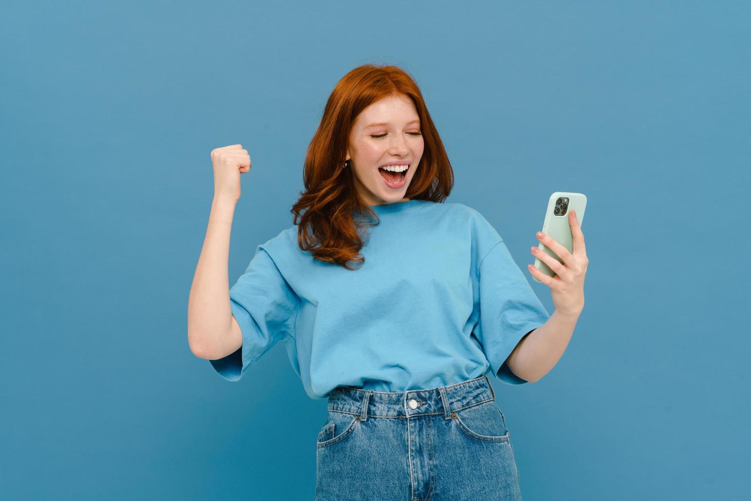 donna eccitata dello zenzero in maglietta che fa gesti e usa il cellulare foto