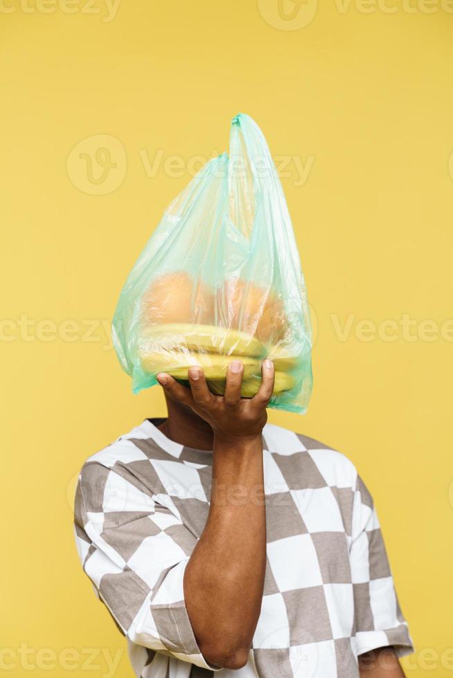 uomo che tiene il sacchetto della spazzatura di plastica con frutta davanti al viso foto