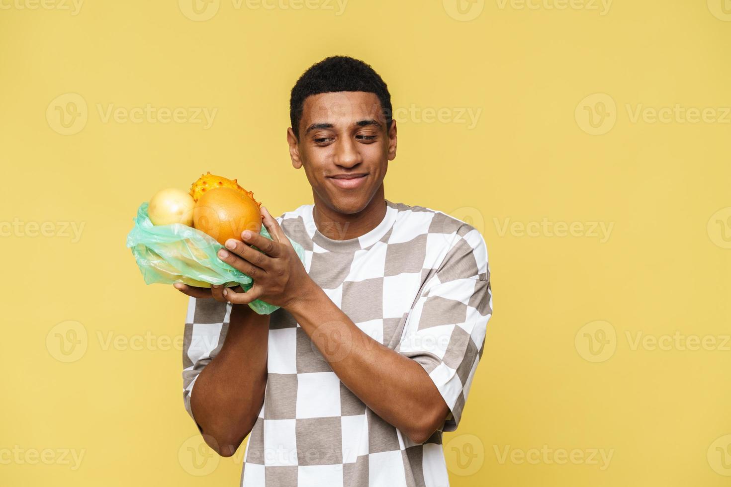 uomo africano sorridente che guarda la frutta nel sacchetto della spazzatura di plastica foto