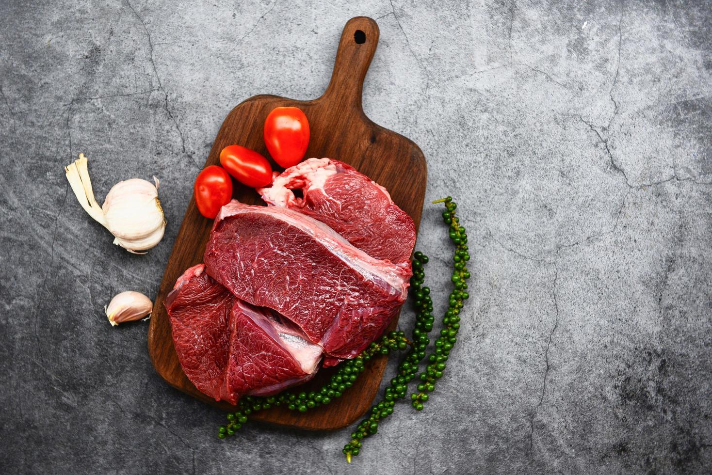 proteine animali di manzo fresco - carne di manzo cruda su tagliere di legno sul tavolo della cucina per cucinare bistecca di manzo arrostita o grigliata con ingredienti erbe e spezie foto