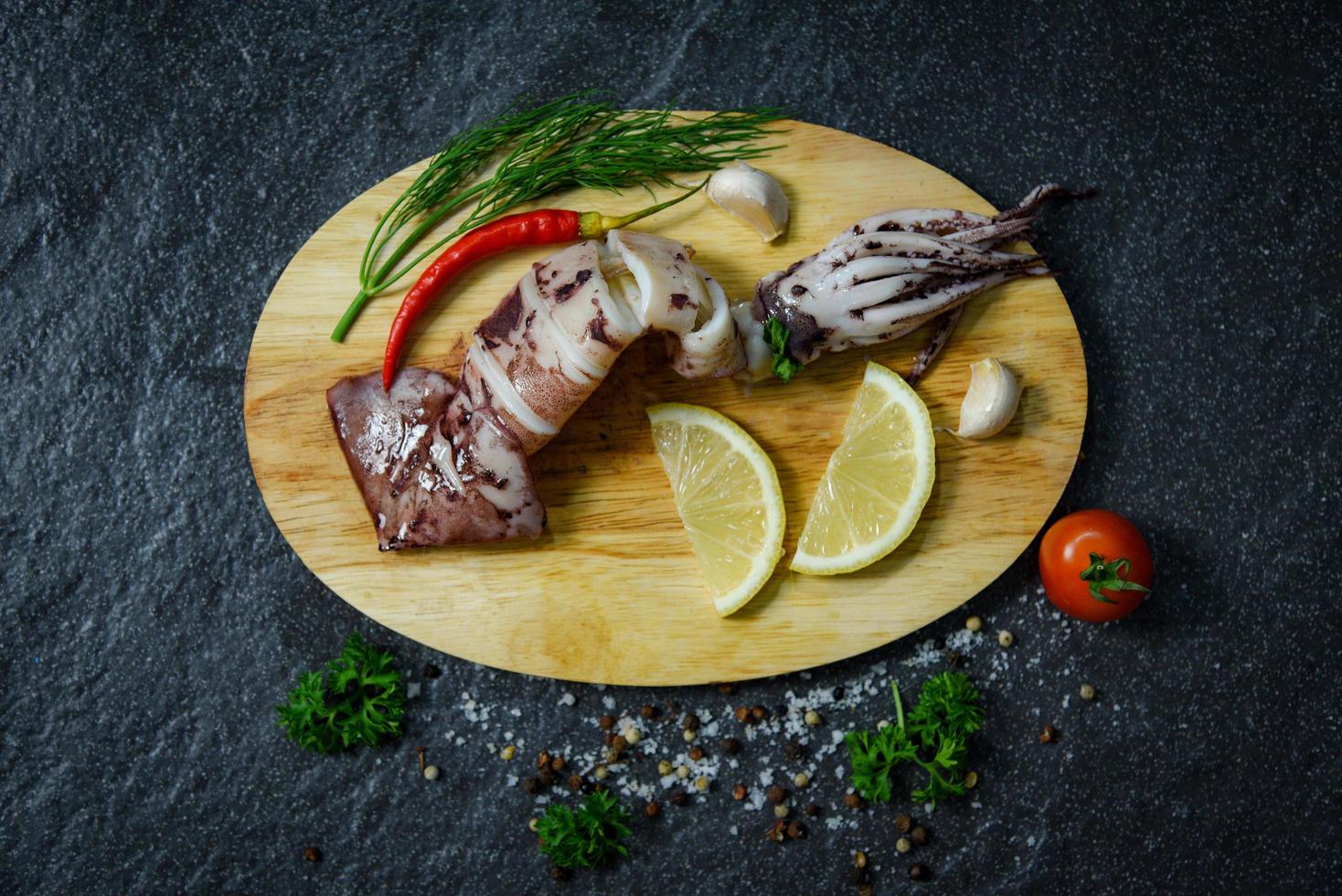 calamari alla griglia di mare con erbe e spezie limone pomodoro peperoncino aglio e aneto sul tagliere foto