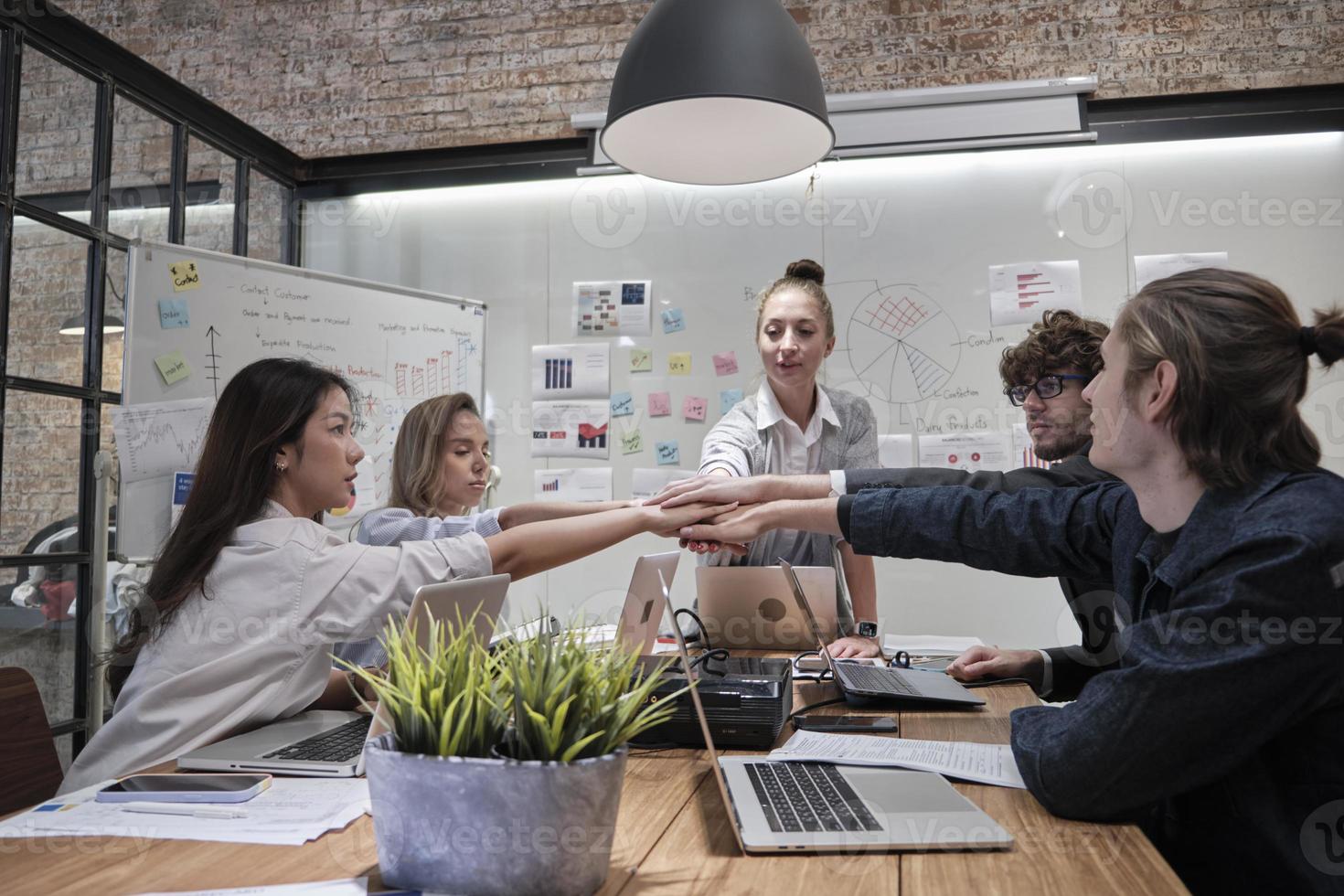 gruppo di colleghi multirazziali lavoro di squadra di brainstorming e solidarietà unendo le mani insieme alla leader donna caucasica per il potere e il successo sindacale dell'azienda in una sala riunioni di un ufficio commerciale. foto