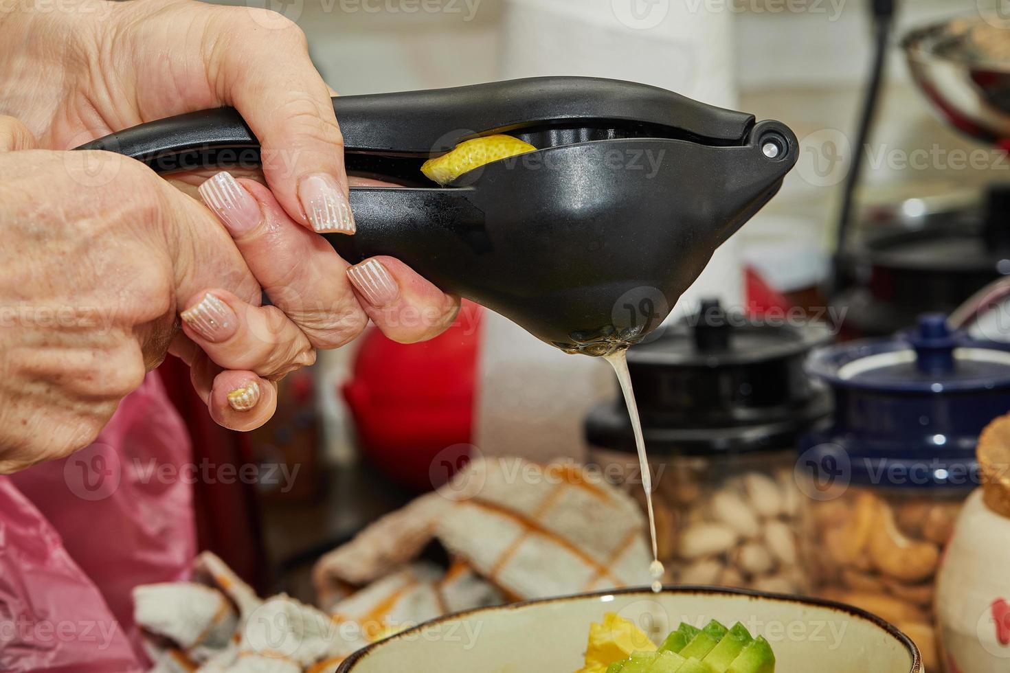 il cuoco spreme il succo di limone nell'insalata usando un dispositivo speciale per preparare l'insalata foto