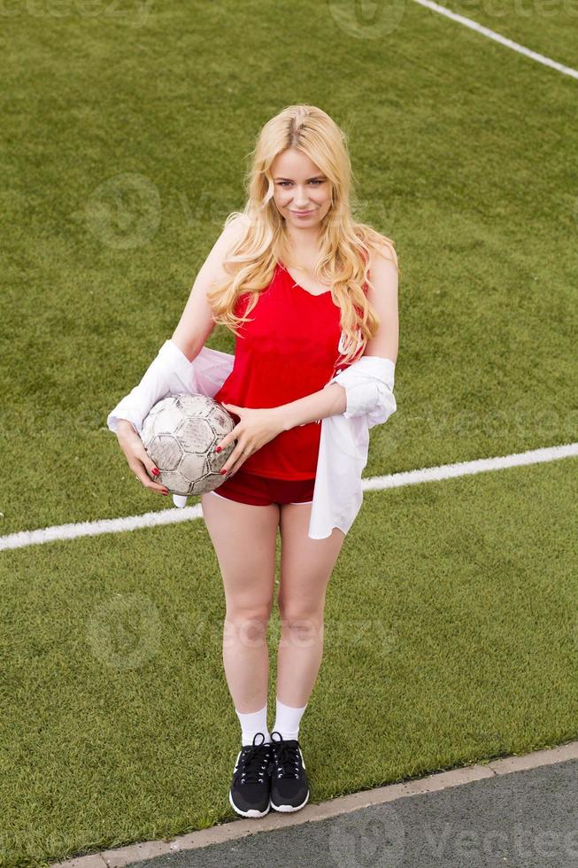 bionda con una palla sul campo di calcio in divisa rossa. foto