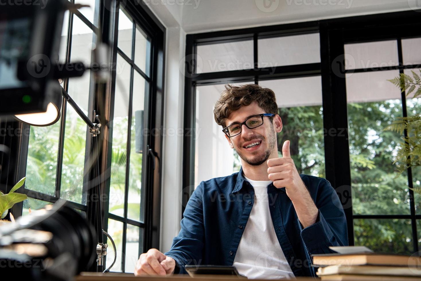 sorridente uomo caucasico vlogger che dà i pollici in su durante la registrazione di video clip con carmera a casa da condividere sui social media foto