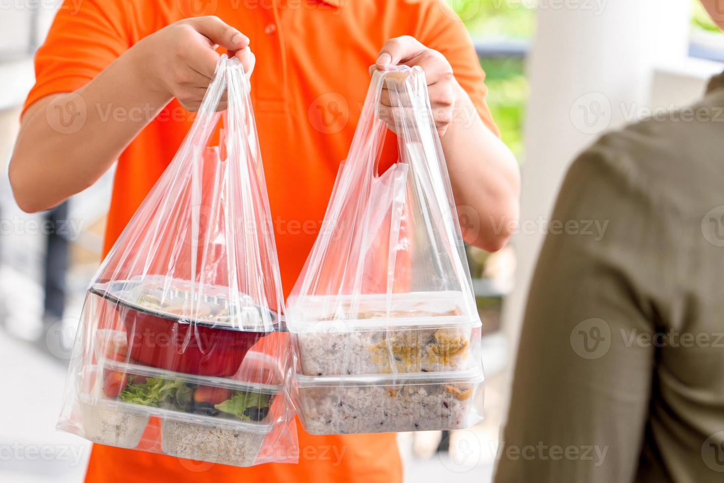 fattorino in uniforme arancione che consegna scatole di cibo asiatico in sacchetti di plastica a un cliente a casa foto