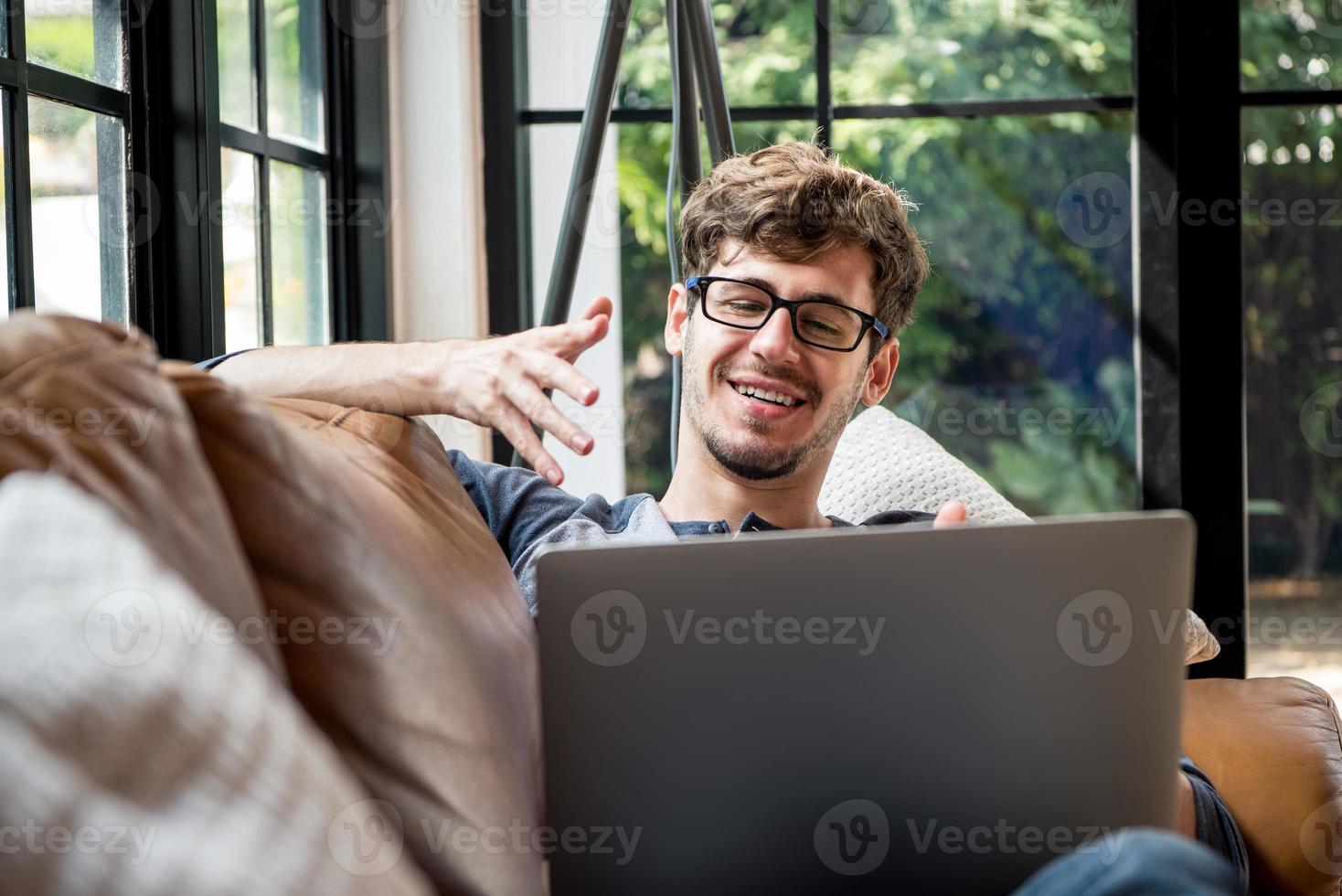 giovane uomo caucasico felice che chatta online tramite videochiamata con un computer portatile sul divano di casa foto