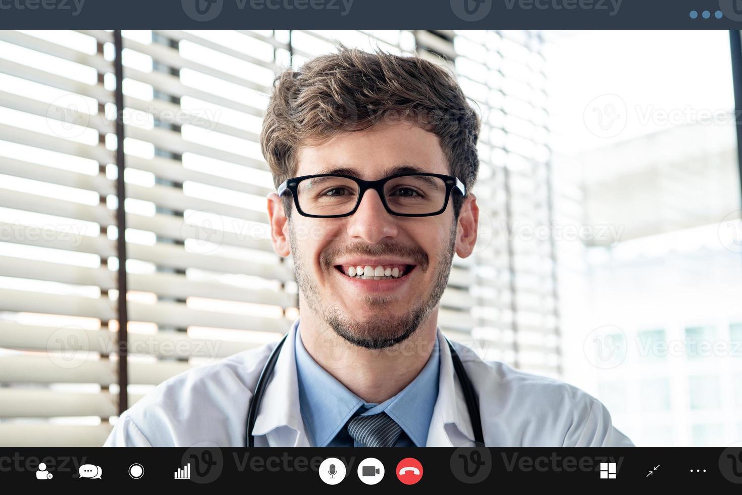 giovane medico che sorride alla telecamera mentre effettua una videochiamata con il paziente online, concetti di servizio di consulenza medica a domicilio foto