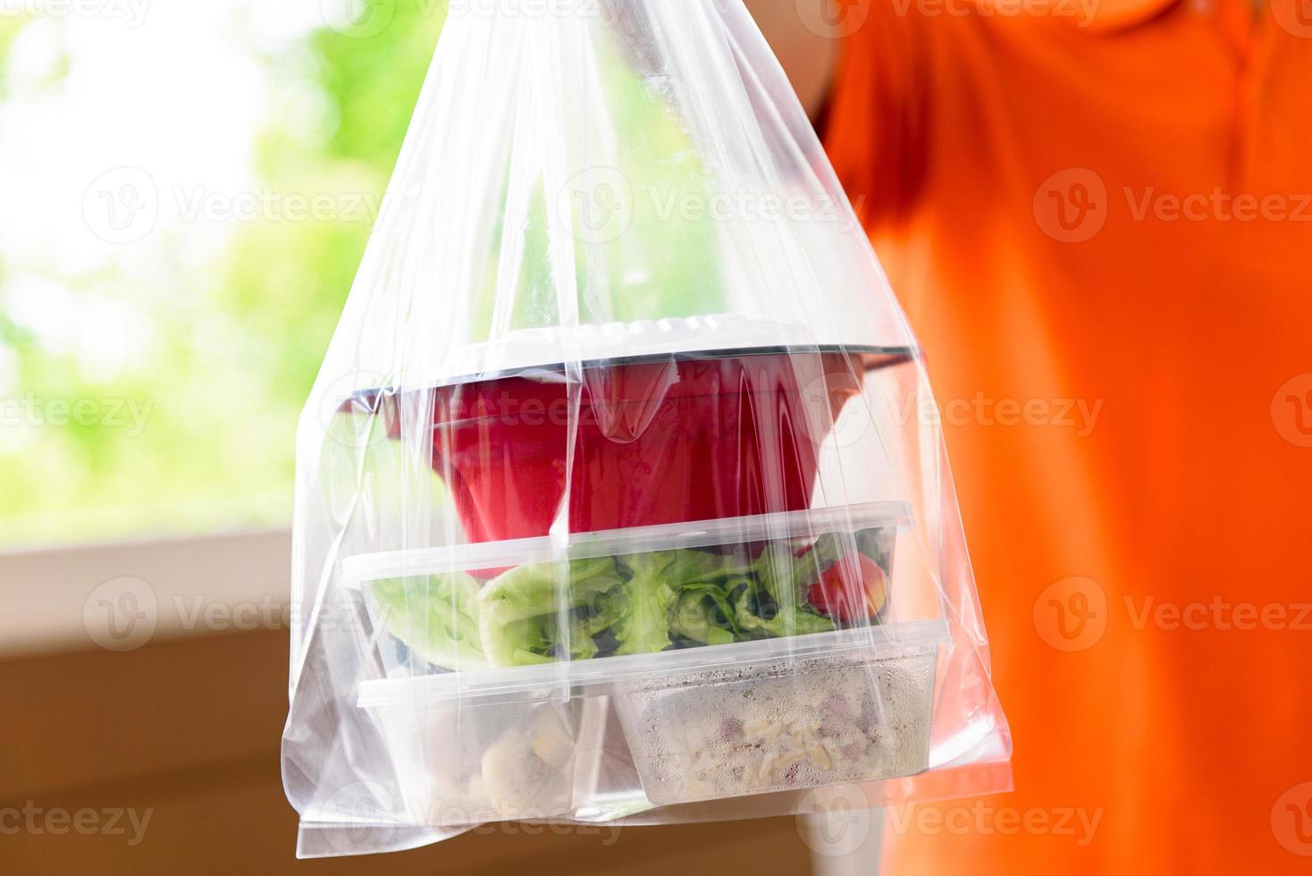 scatole di cibo asiatico in sacchetti di plastica consegnate al cliente a casa dal fattorino in uniforme arancione foto