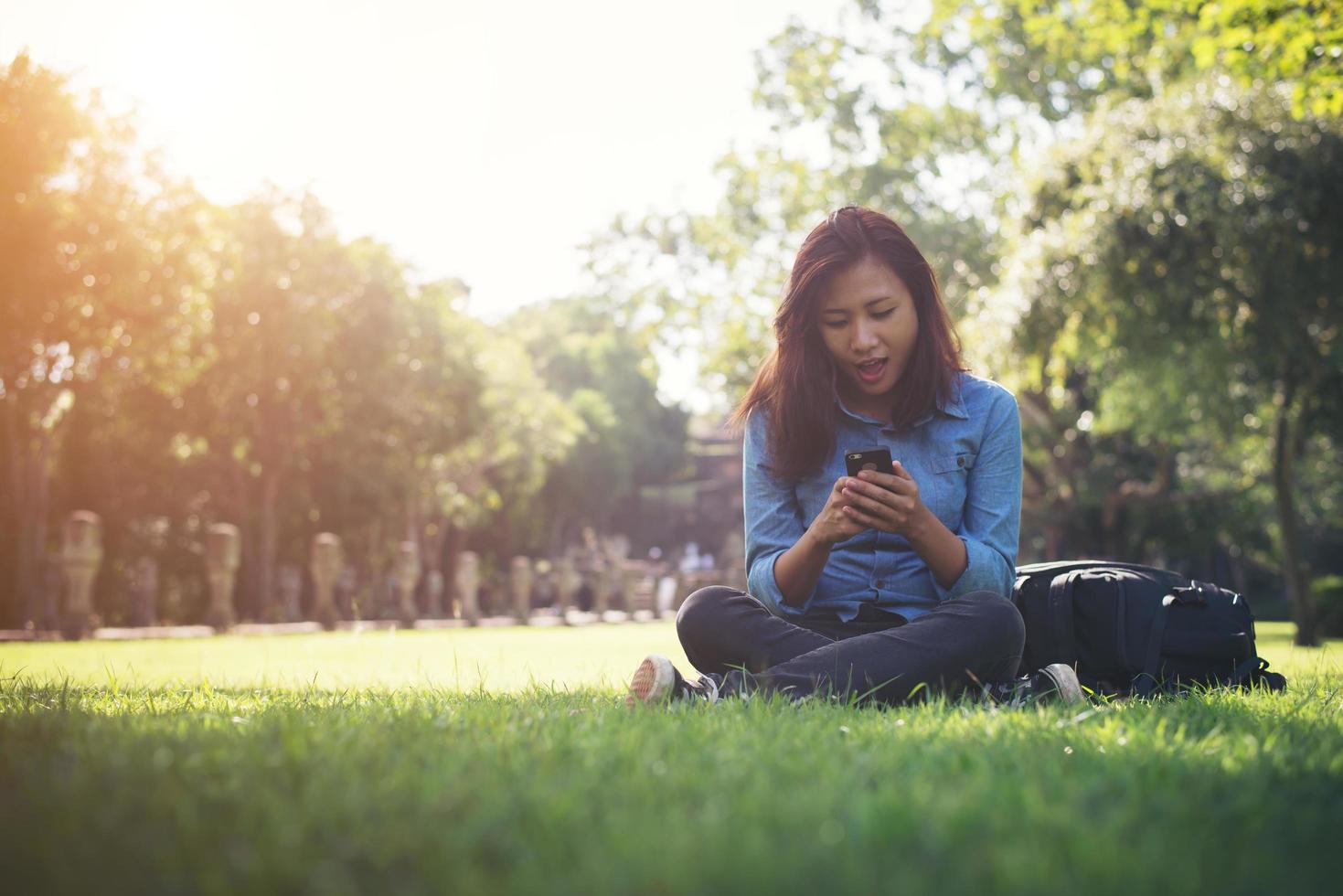 giovane donna hipster che digita sul suo telefono mentre è seduto al parco verde. foto