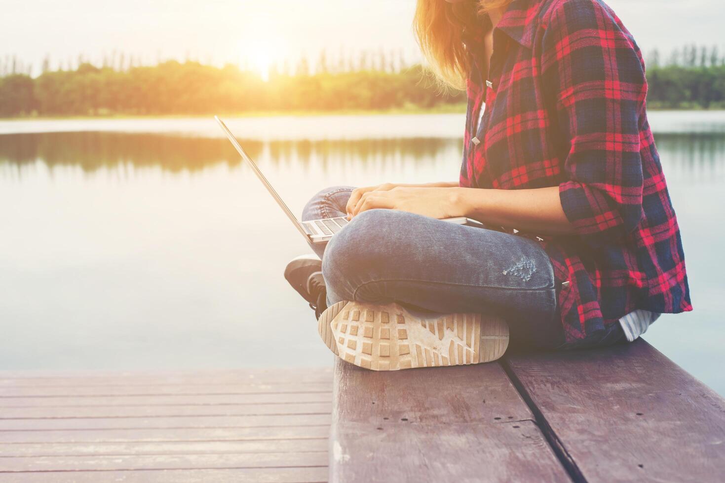 giovane donna felice hipster che lavora con il suo computer portatile seduto sul molo, rilassante godere con la natura. foto