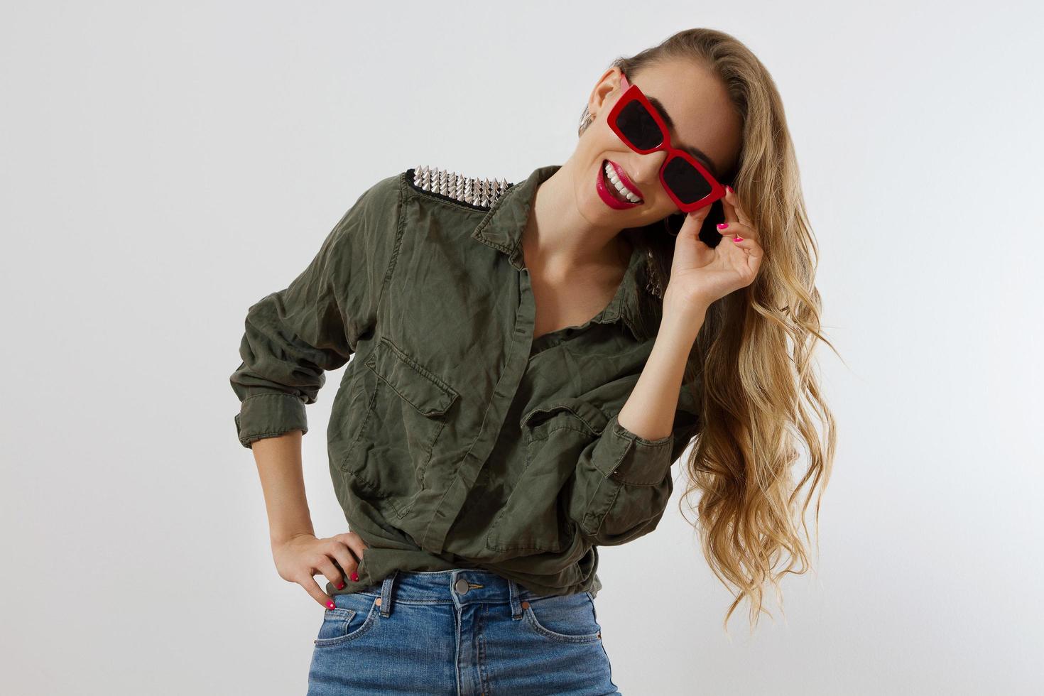 donna elegante con gli occhiali rossi che guarda l'obbiettivo in studio isolato su sfondo bianco. copia spazio. stile alla moda del bellissimo modello di lusso con trucco labbra rosse. lunghi capelli biondi lucidi ondulati foto