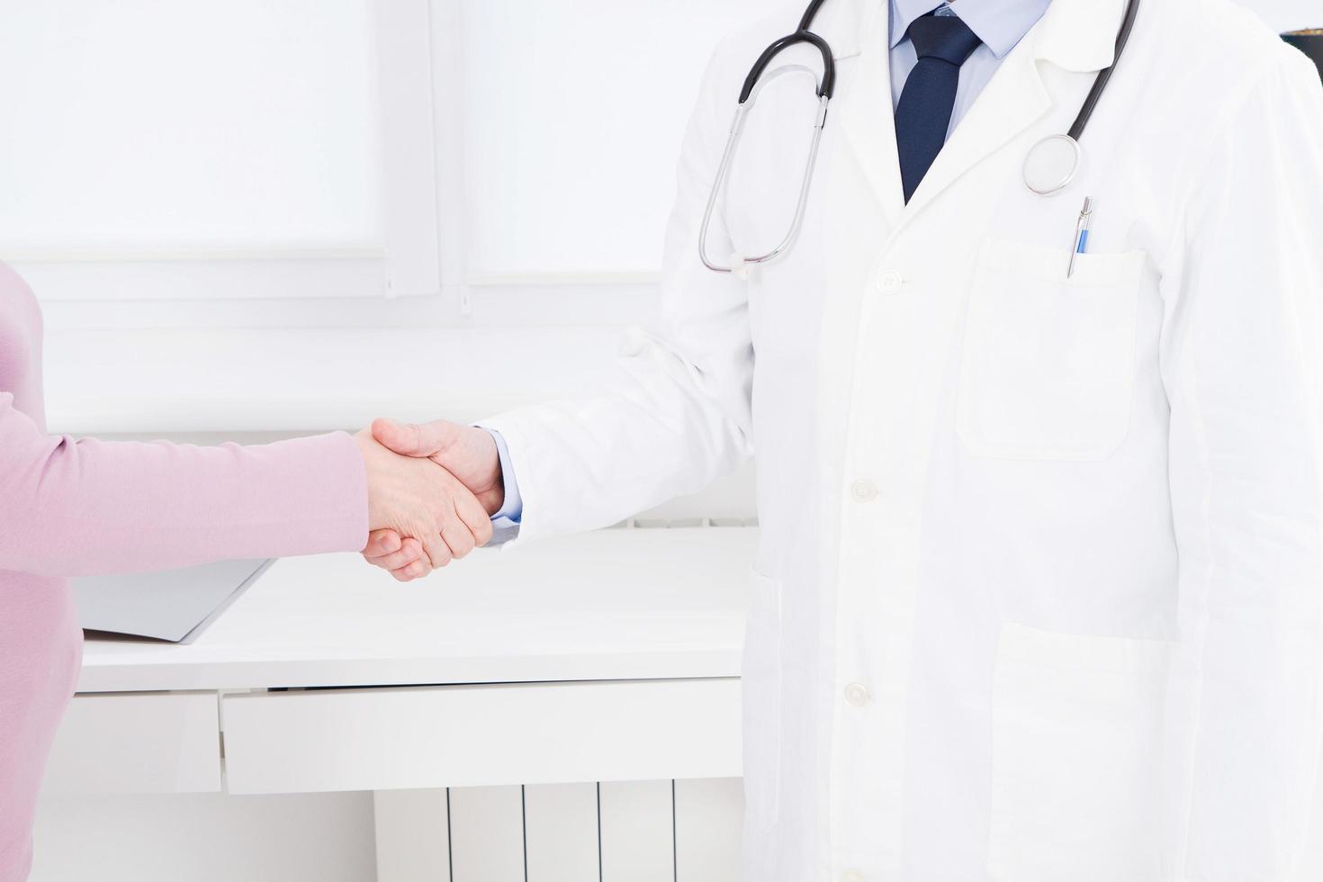 la mano maschile del medico scuote il braccio femminile del suo paziente in clinica, studio medico. concetto di assistenza sanitaria, assicurazione sanitaria foto