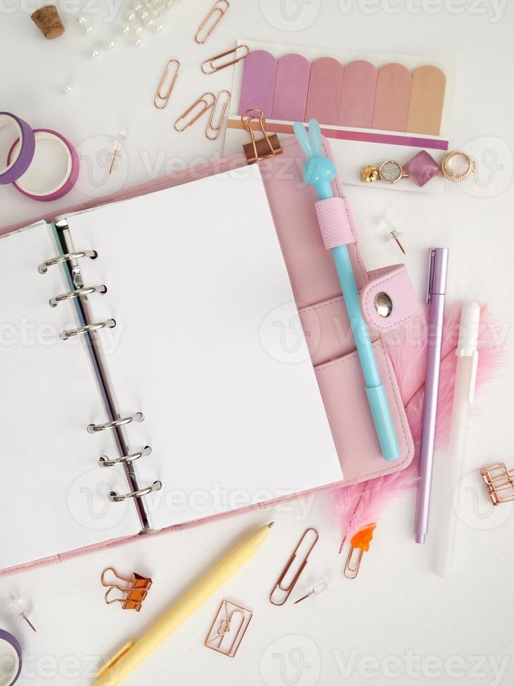 il diario si apre con una pagina bianca e olografica. agenda rosa con graziosi articoli di cancelleria che fotografano in stile flatlay. vista dall'alto del pianificatore rosa con cancelleria aziendale foto