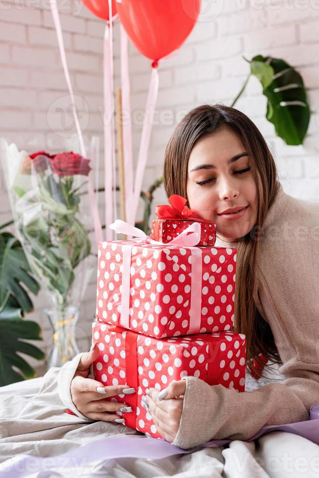 giovane donna seduta nel letto per celebrare il giorno di San Valentino che abbraccia un mucchio di regali foto