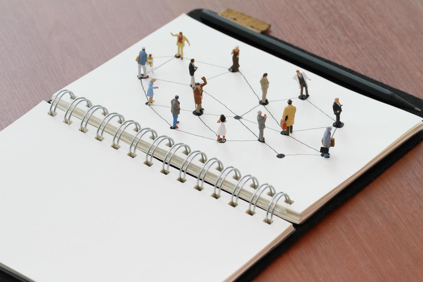 primo piano di persone in miniatura con diagramma di rete sociale su taccuino aperto su scrivania in legno come concetto di social media foto