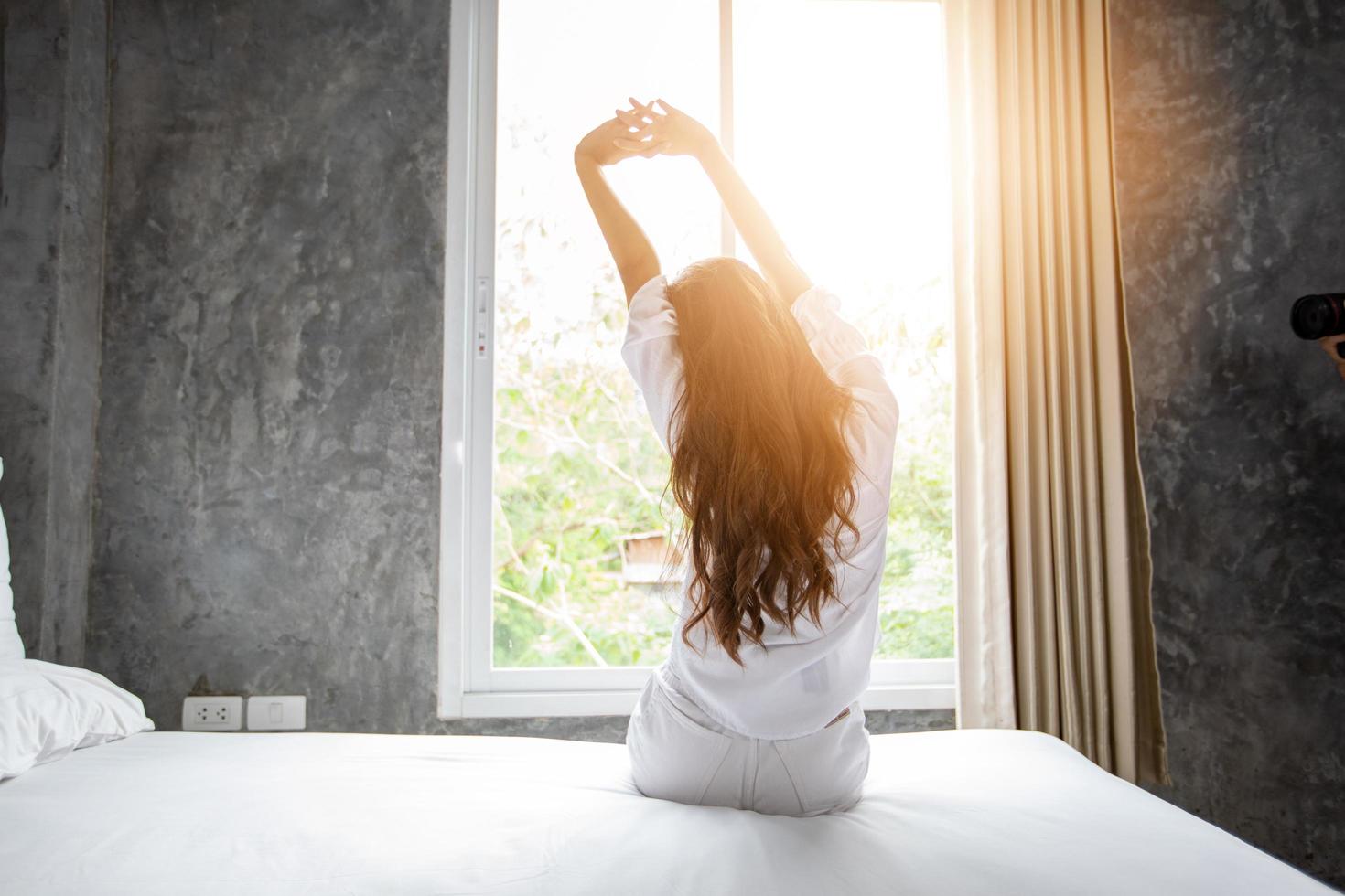 donna asiatica che si sveglia nel suo letto completamente riposata e apre le tende al mattino per prendere aria fresca. foto