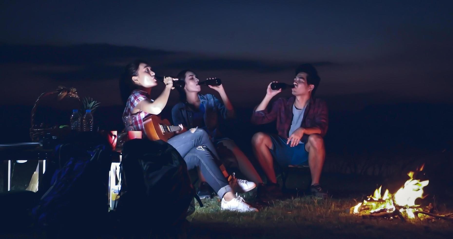 un gruppo di turisti asiatici che bevono e suonano la chitarra insieme alla felicità in estate mentre si accampano vicino al lago al tramonto foto