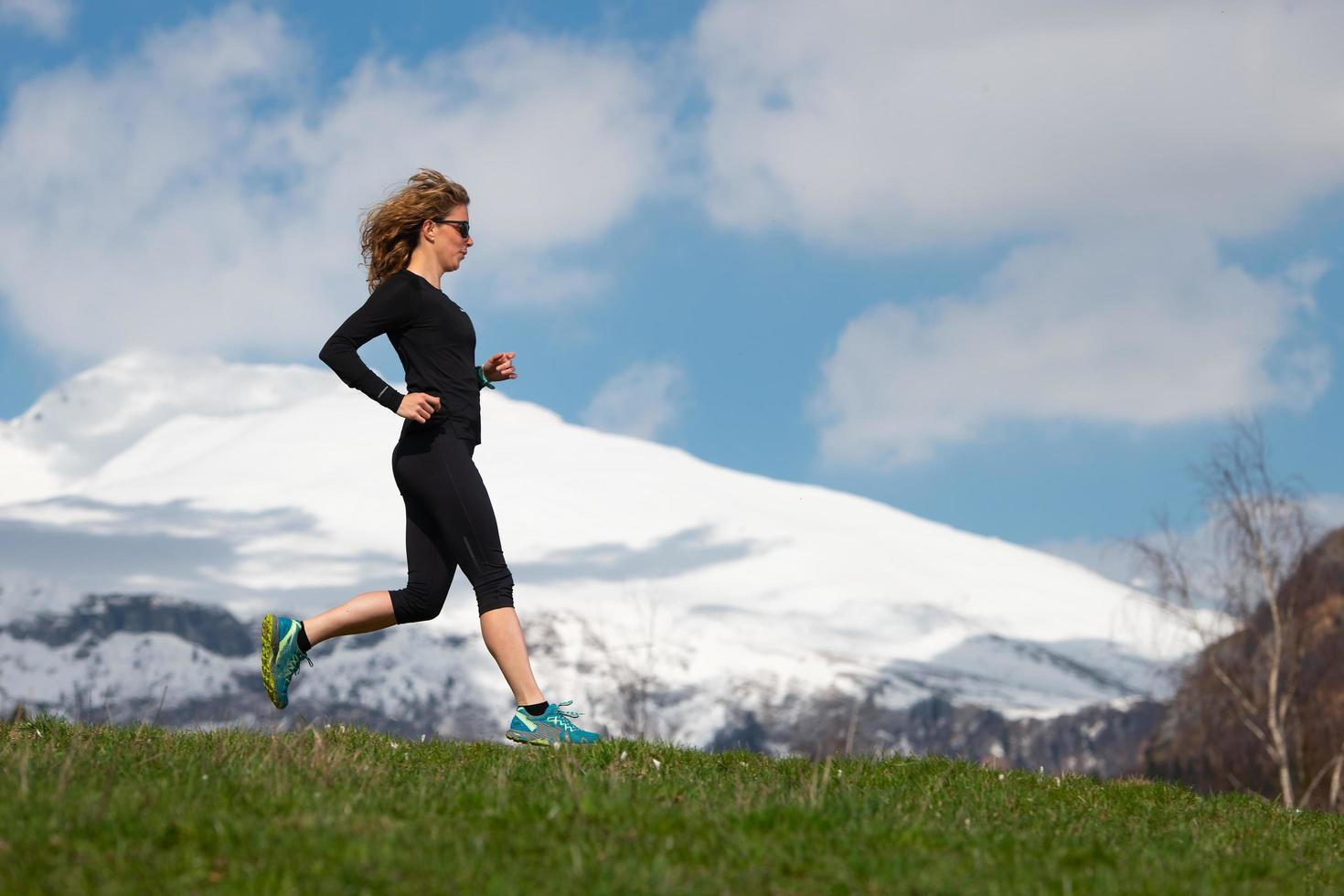 ragazza atleta corre in montagna sul prato primaverile con montagne di neve sullo sfondo foto