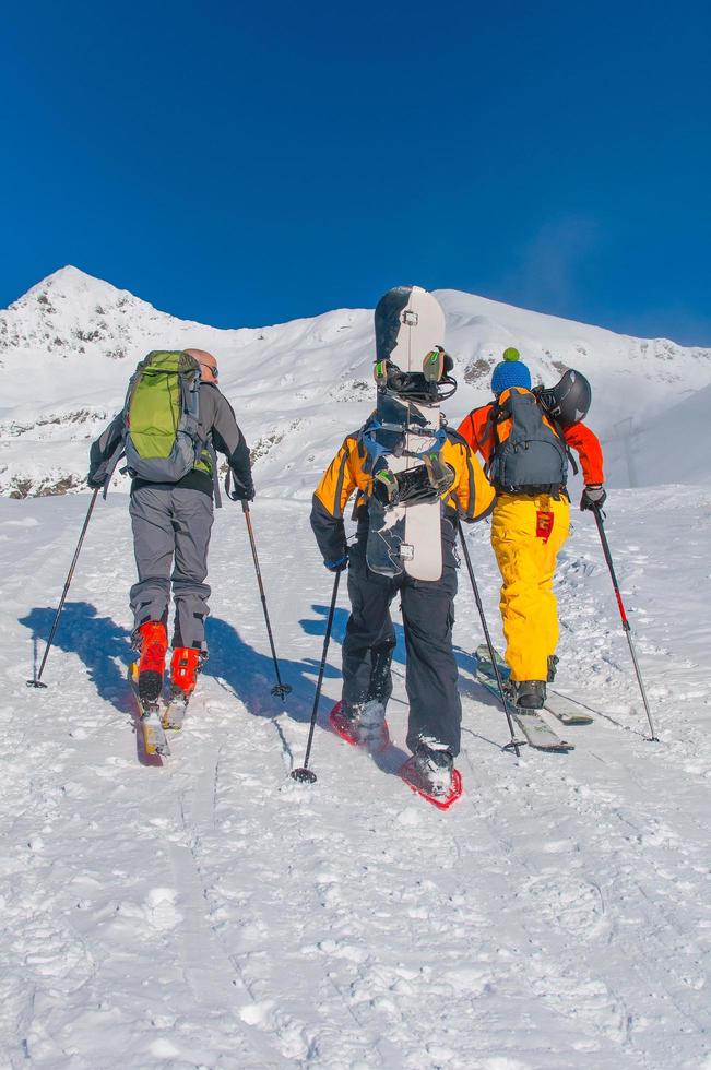 amici con sci e snowboard salgono la collina con ciaspole e pelli di foca foto